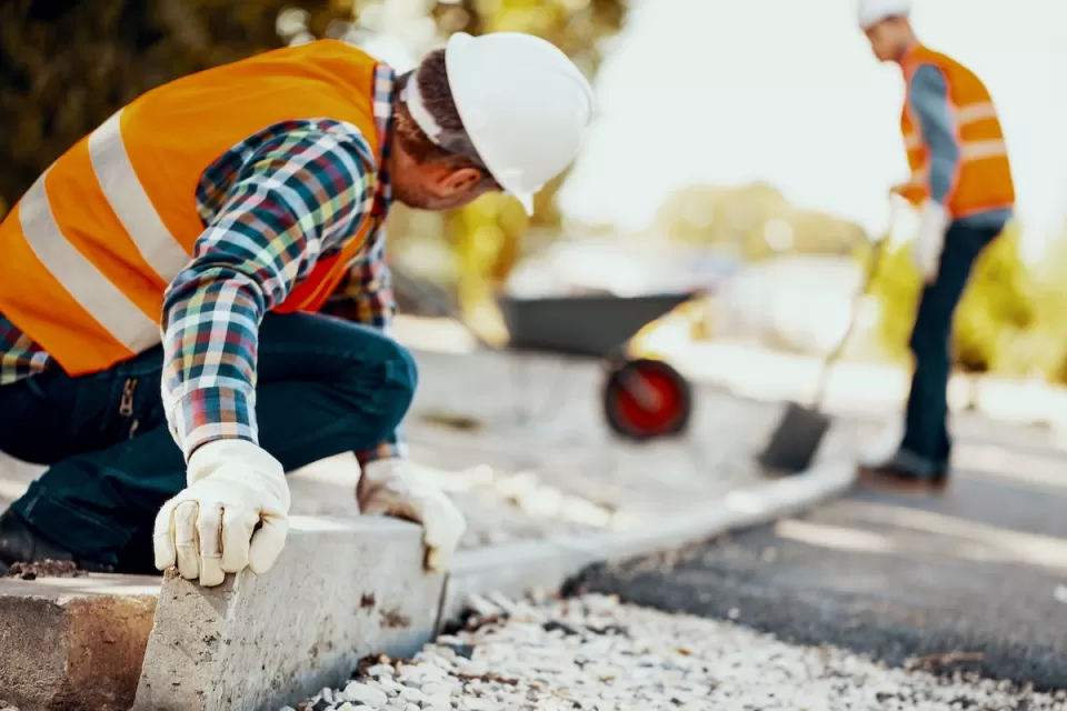 Construction workers in orange vests and white hard hats installing concrete curb.